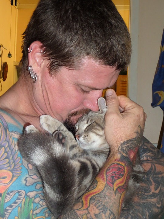 Tattood man hugging kitten